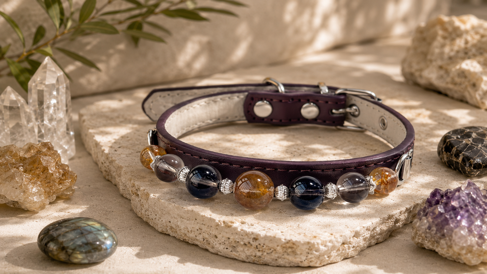 A purple leather collar with silver hardware and a beaded band featuring dark blue, amber, and clear gemstones, displayed on a stone slab surrounded by crystals.